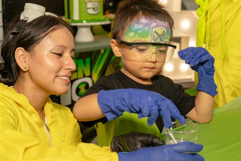 Niño cumpleañero con guantes y gafas haciendo un experimento junto a la animadora