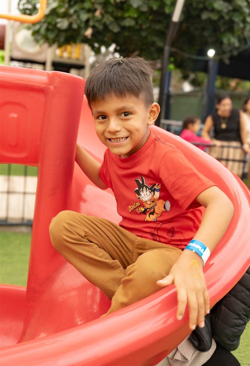 Niño sonriendo en un tobogán rojo durante una fiesta infantil