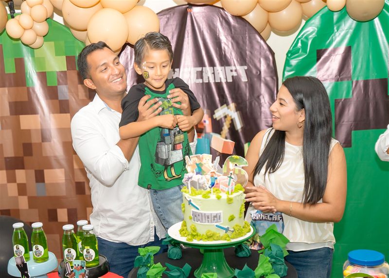 Niño de seis años soplando la vela de su torta de Minecraft junto a sus padres