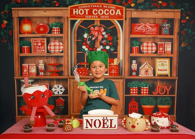 Niño con gorro de cocinero verde decorando una galleta con manga pastelera en el set navideño