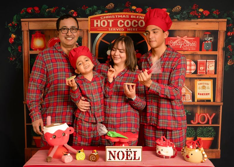 Familia con pijamas navideñas a cuadros y gorros de cocinero decorando galletas
