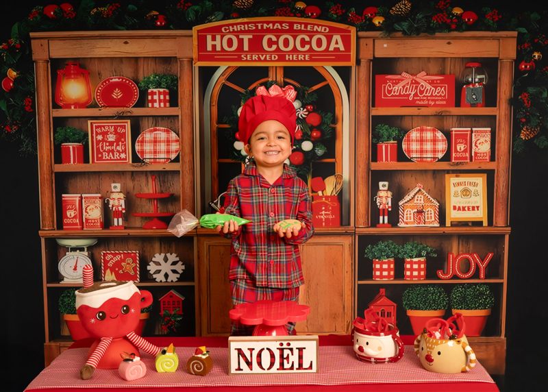 Niño sonriente con pijama navideña y gorro de cocinero mostrando su galleta decorada