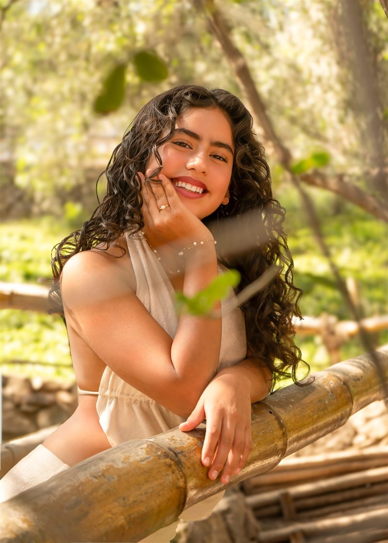 Retrato de una joven de cabello rizado sonriendo sobre una baranda de bambú