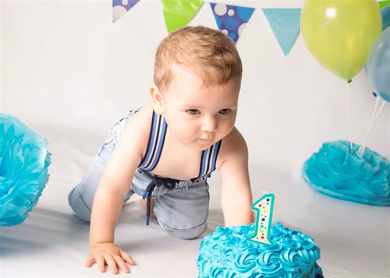Bebé gateando hacia su pastel azul con el número 1, globos y banderines