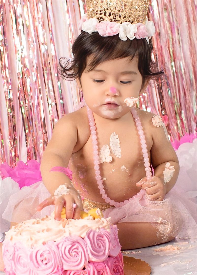 Bebé con corona dorada tocando su pastel de rosas rosadas